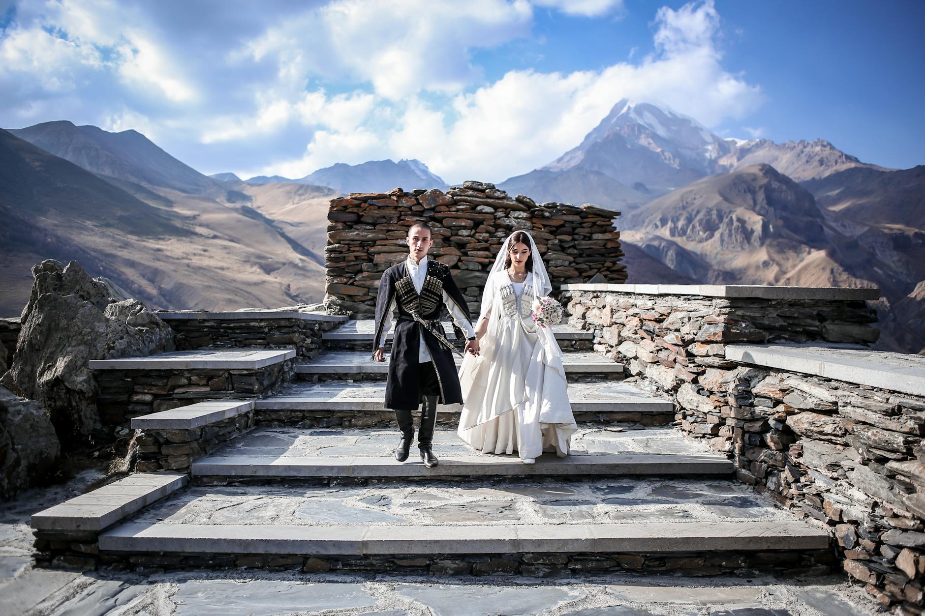 Para młoda w góralskich strojach schodzi po kamiennych schodach w górach